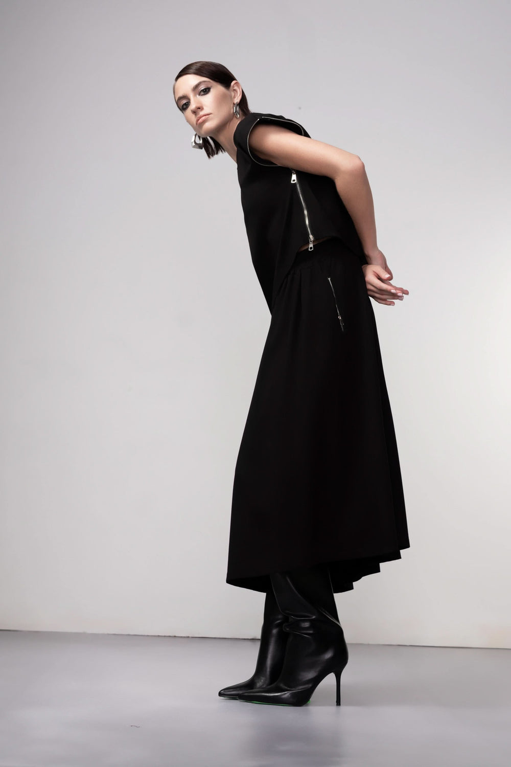 Modèle portant une jupe midi coupe fluide noire avec talons, accentuant le mouvement et l'élégance asymétrique.