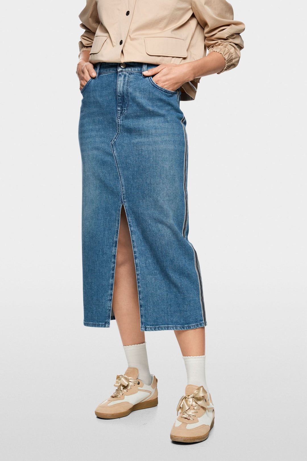 Jupe midi en jean à rayures latérales avec fente avant, portée avec une veste beige et baskets beiges, style décontracté chic.