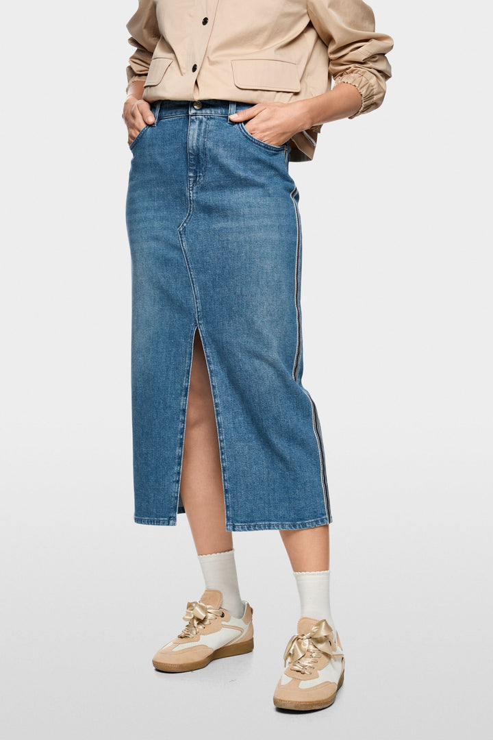Jupe midi en jean à rayures latérales avec fente avant, portée avec une veste beige et baskets beiges, style décontracté chic.