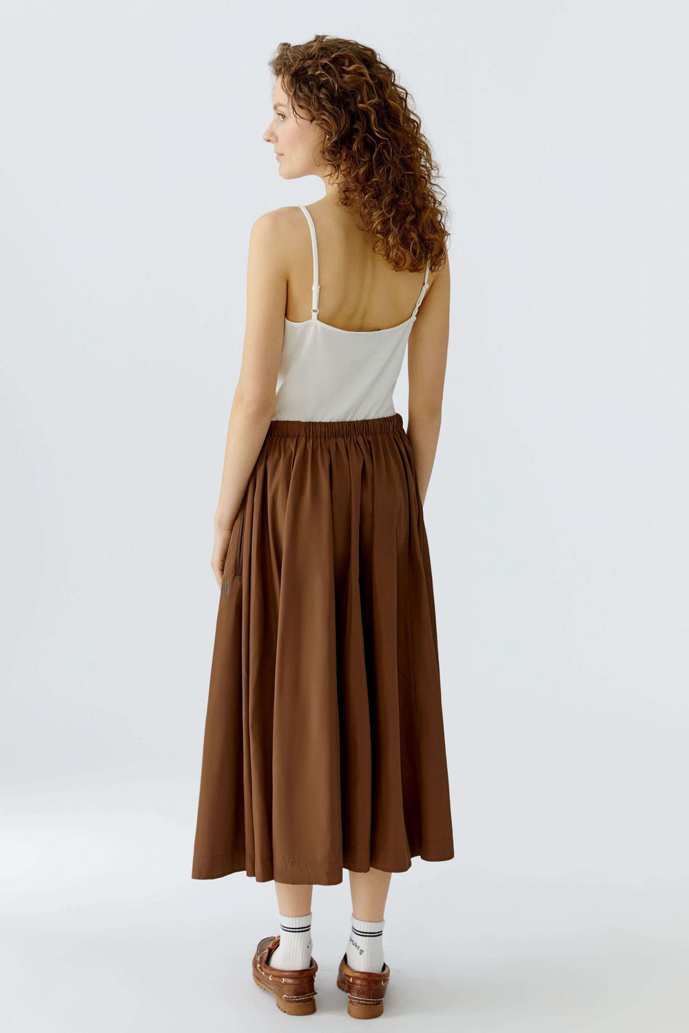 Jupe midi fluide marron avec taille élastique et cordon, offrant confort et mouvement naturel, portée avec un haut blanc simple.