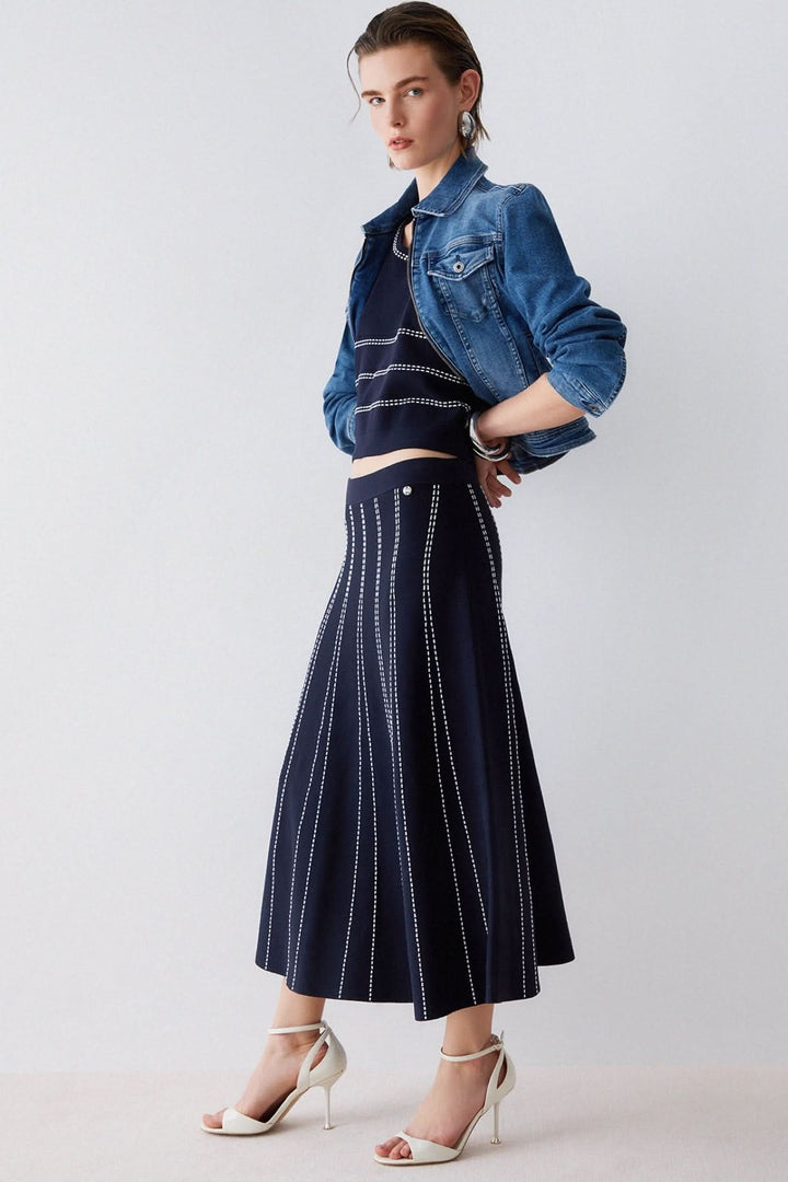 Femme portant une jupe midi évasée à motif rayé, associée à une veste en jean et des talons hauts, look élégant et moderne.