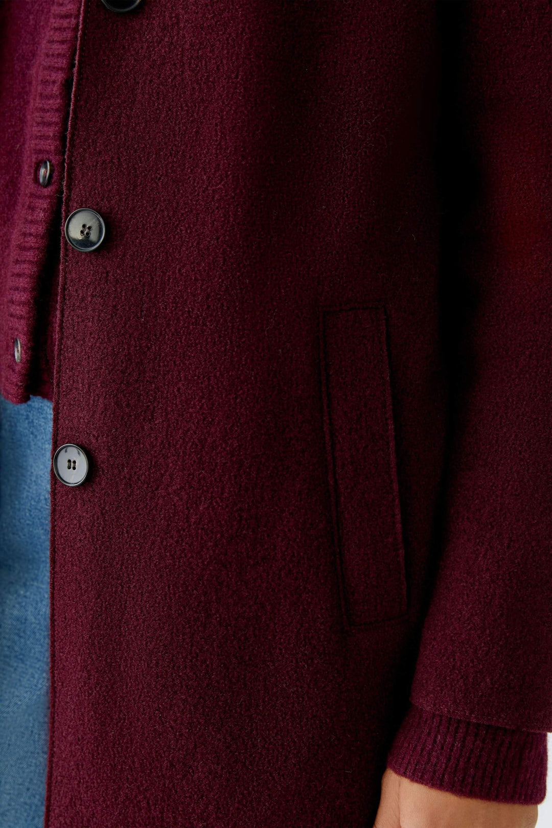 Détail d'un manteau Mayson, long et droit, en tissu bordeaux avec boutons et poches.