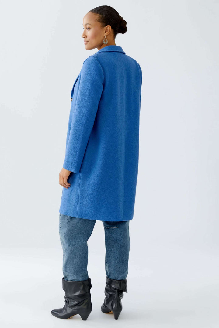 Manteau Mayson bleu sur modèle féminin, coupe droite et longue, porté avec jean et bottes pour un look chic.