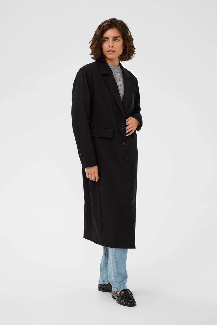 Femme portant le Manteau Milos noir, coupe droite et mi-long, style élégant idéal pour tenues professionnelles et décontractées.