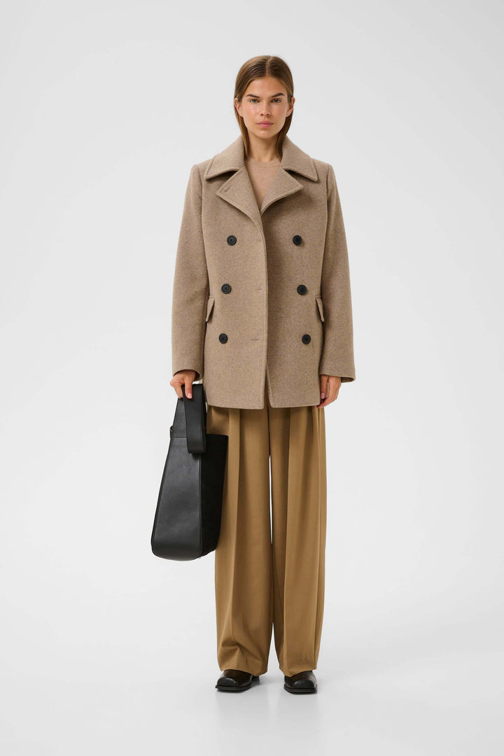 Femme portant un Manteau Perry croisé en laine avec col à larges revers et fermeture à double boutonnage, associée à un pantalon classique.