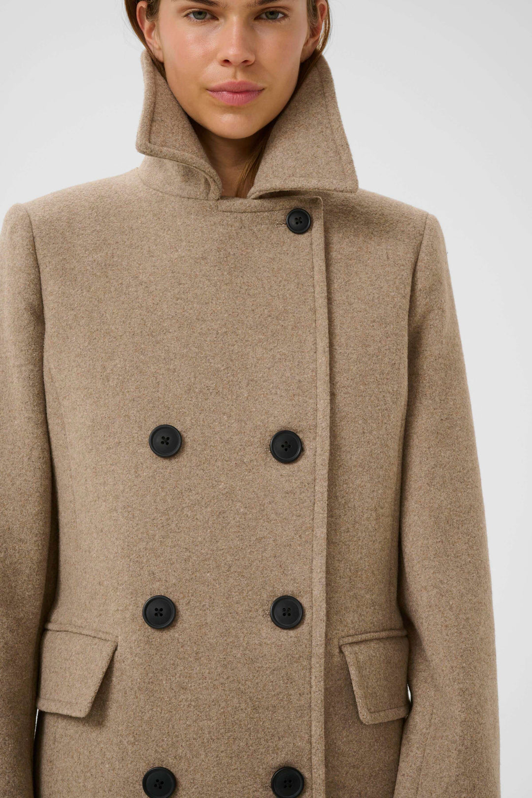 Manteau Perry croisé en laine beige à double boutonnage, col à larges revers, porté par une femme, élégant et intemporel.