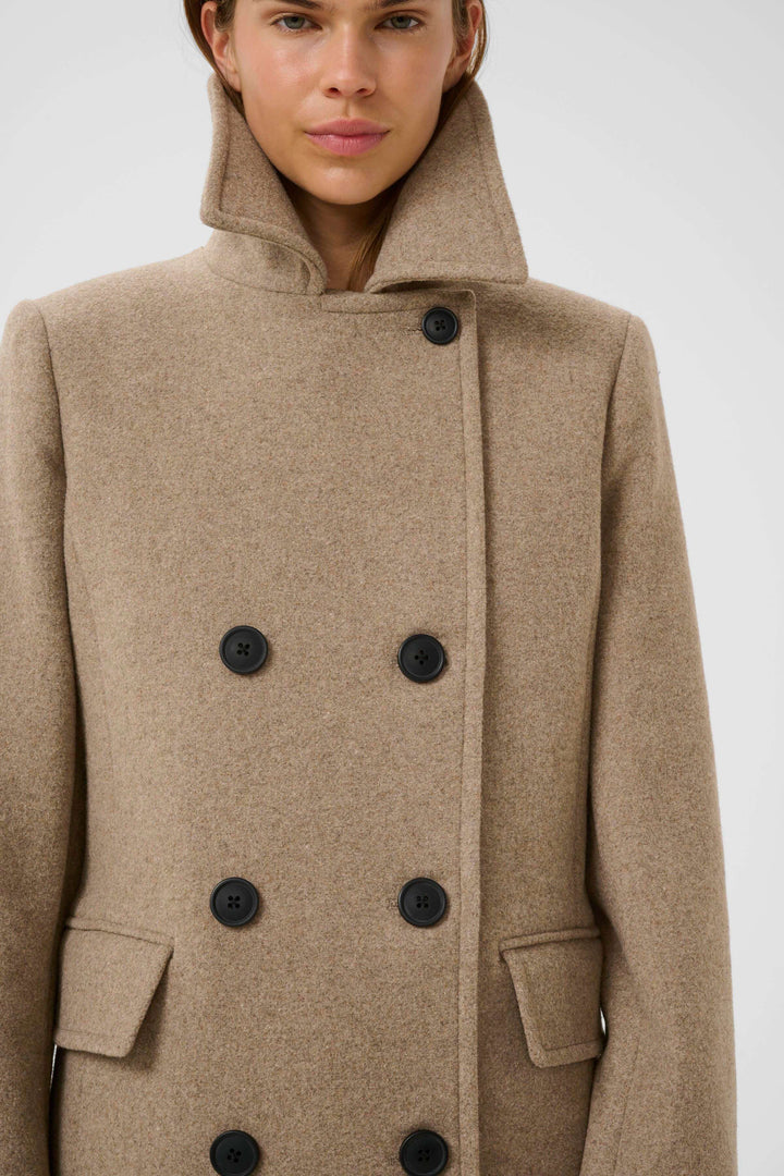 Manteau Perry croisé en laine beige à double boutonnage, col à larges revers, porté par une femme, élégant et intemporel.