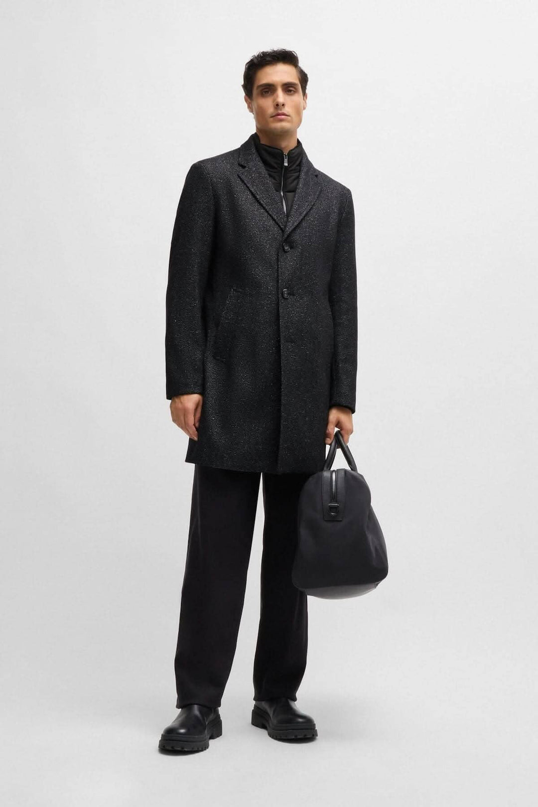 Homme portant un manteau en tweed ajusté BOSS avec fermeture éclair détachable et sac à main noir.
