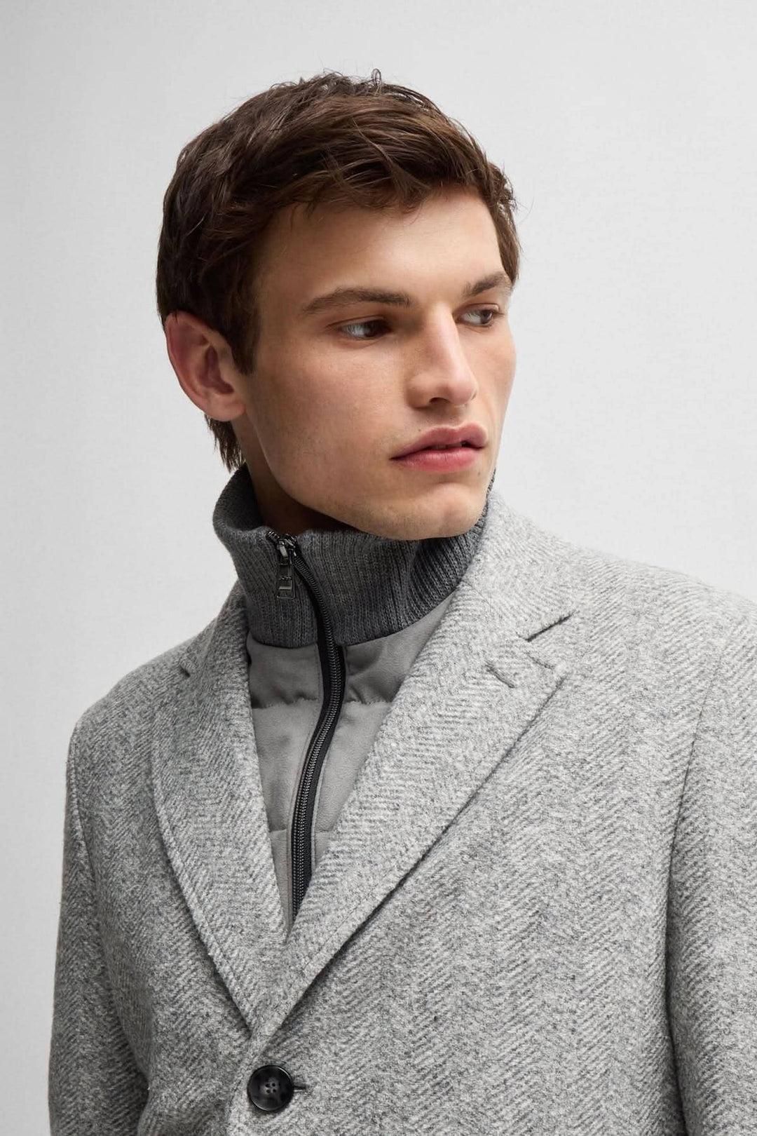 Homme portant un manteau à chevrons gris avec une fermeture éclair amovible, détail sur le col.