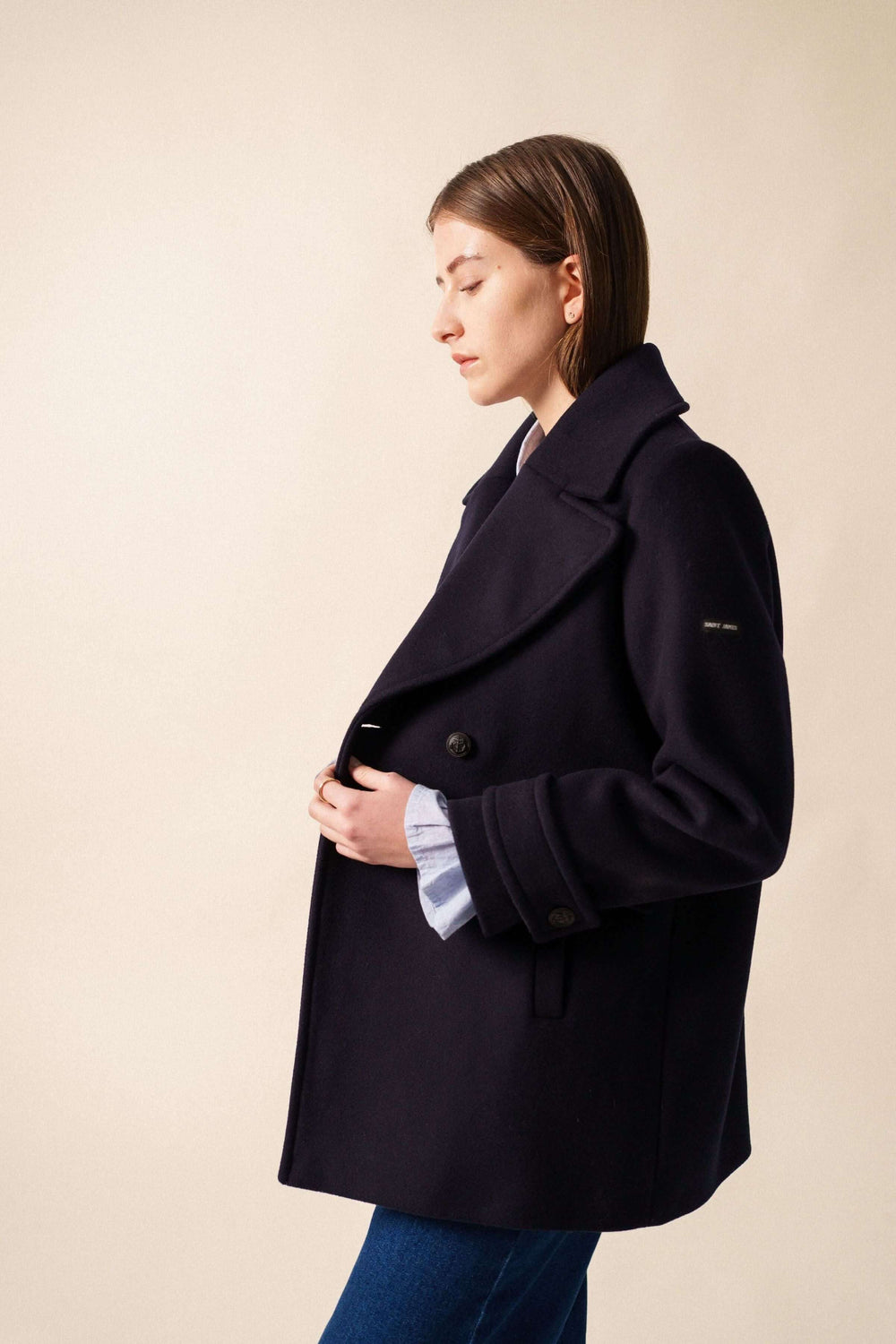 Femme portant le Manteau chic STE ROMY noir, avec encolure en V et grand col, montrant des boutons avant et manches élégantes.