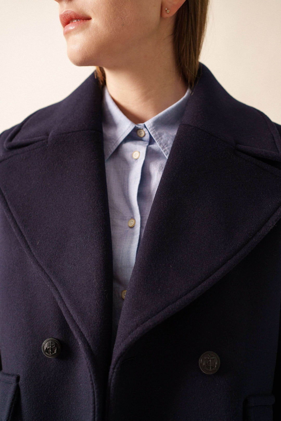 Manteau chic STE ROMY avec col en V et quatre boutons, superposé sur chemise bleu, manche visible, style décontracté et élégant.