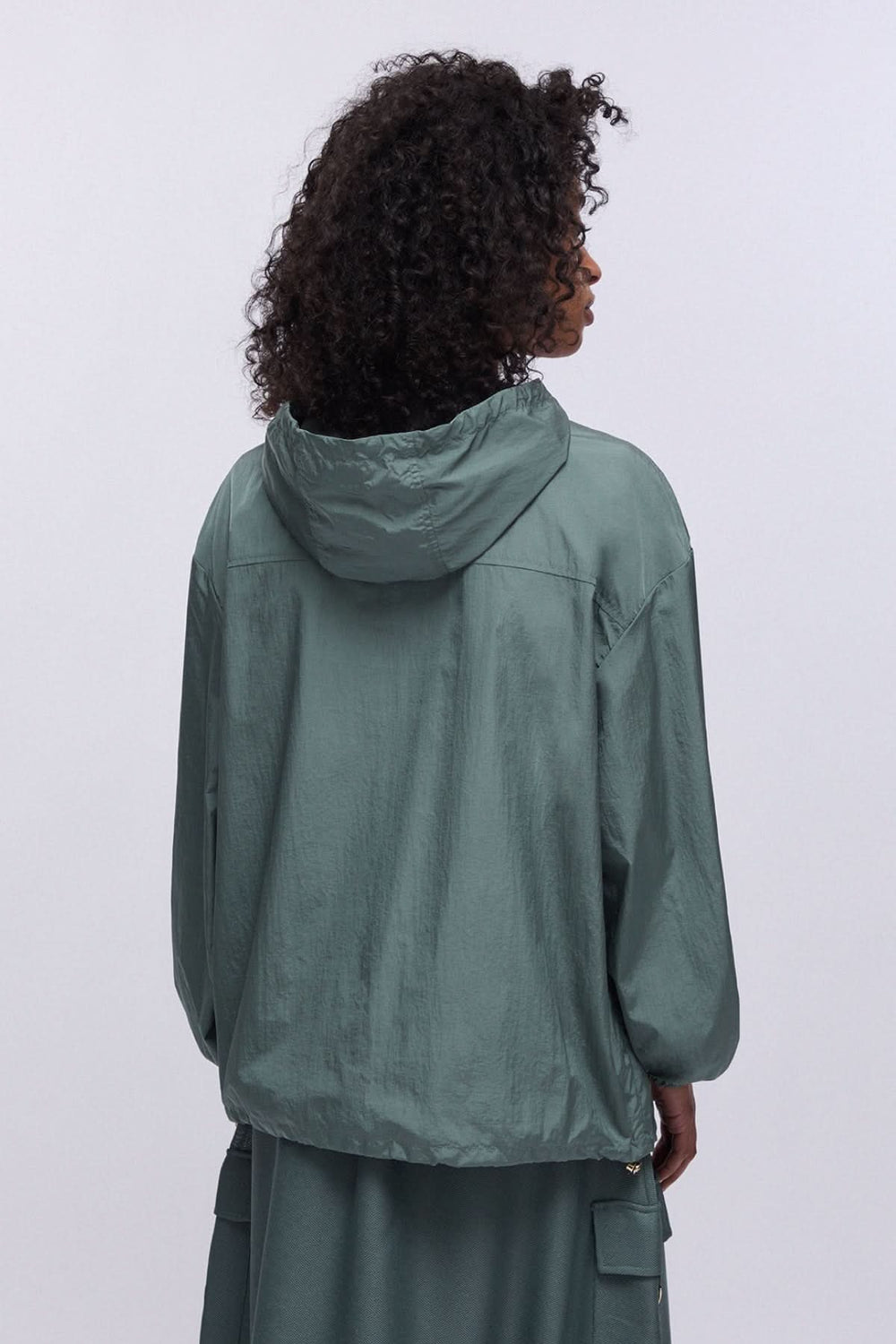 Personne portant un manteau coupe-vent à capuche avec poche poitrine, vue de dos, couleur vert foncé.