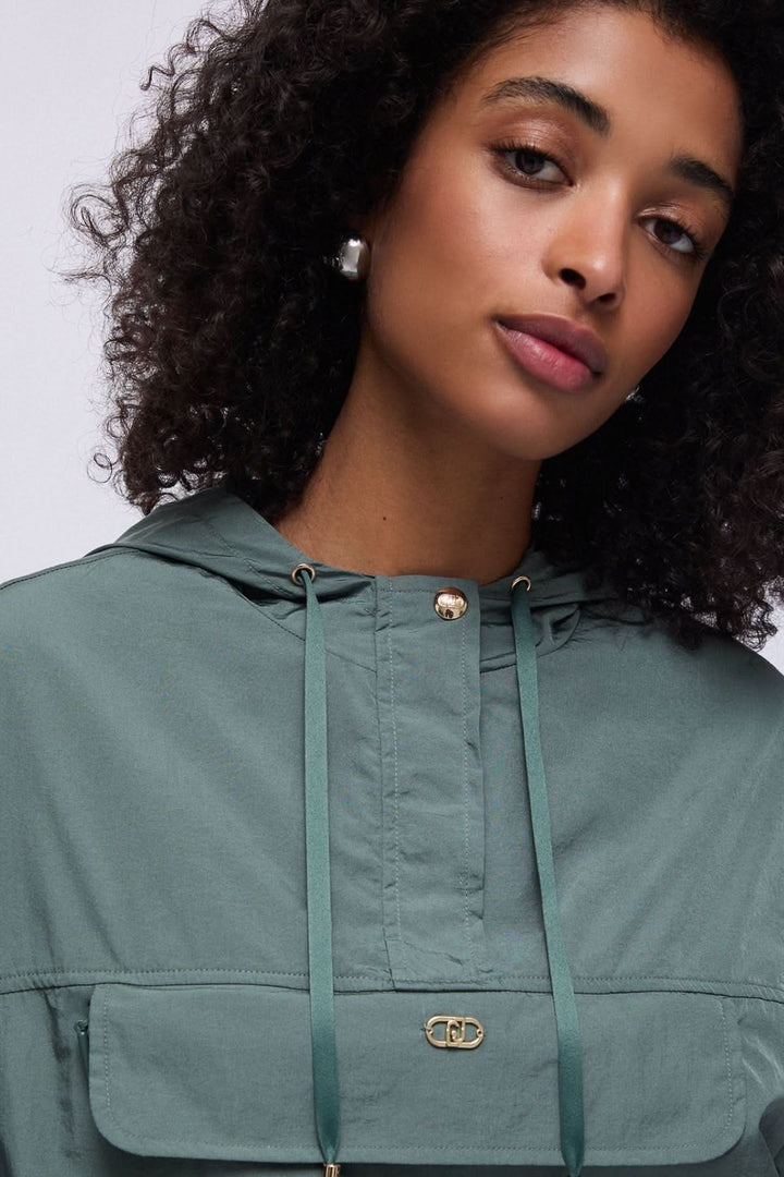 Femme portant un manteau coupe-vent à capuche avec poche poitrine, style moderne et décontracté, idéal pour mi-saison.
