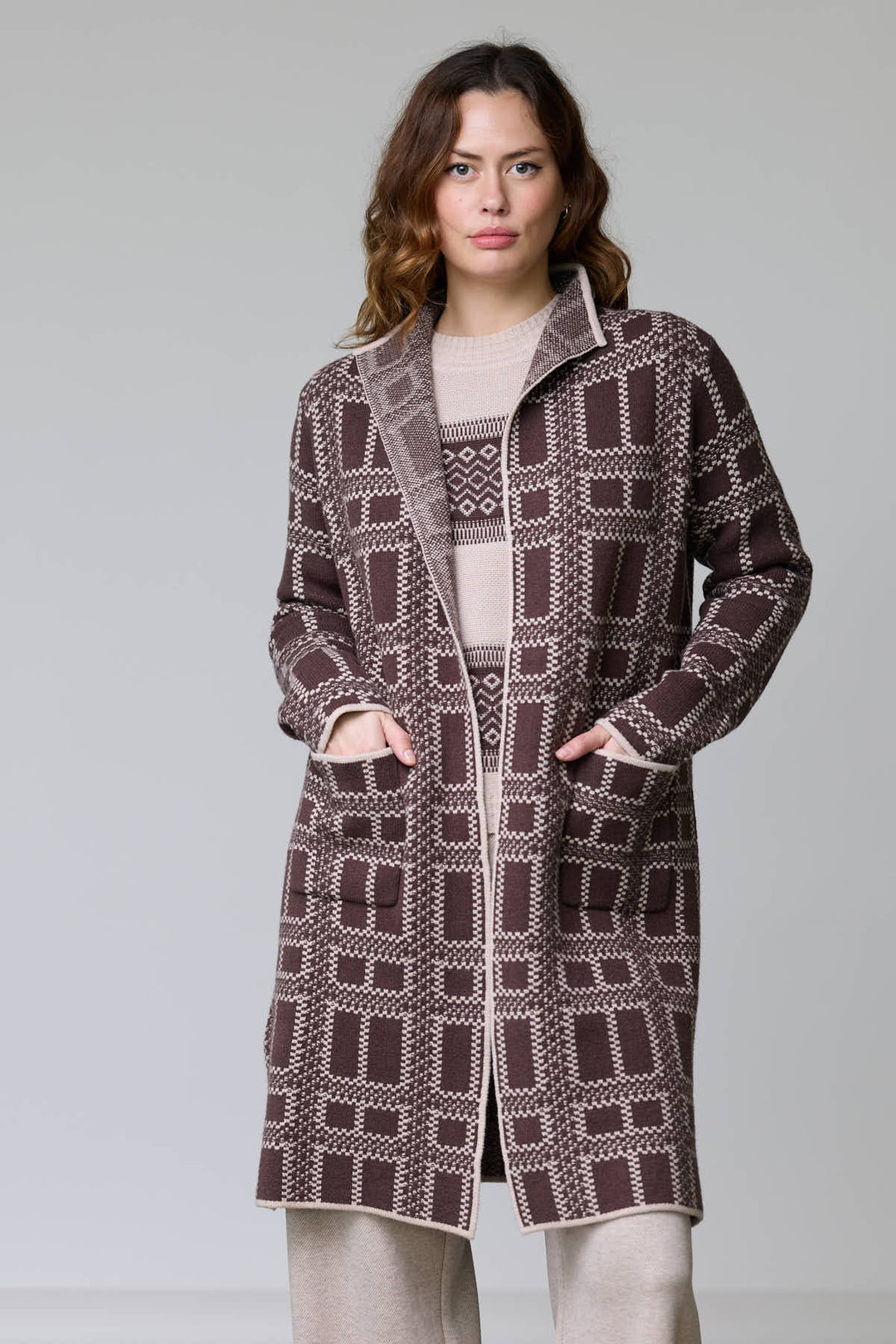 Femme portant un manteau en tricot à motif géométrique avec col ouvert et poches plaquées, coupe droite et finitions contrastantes.