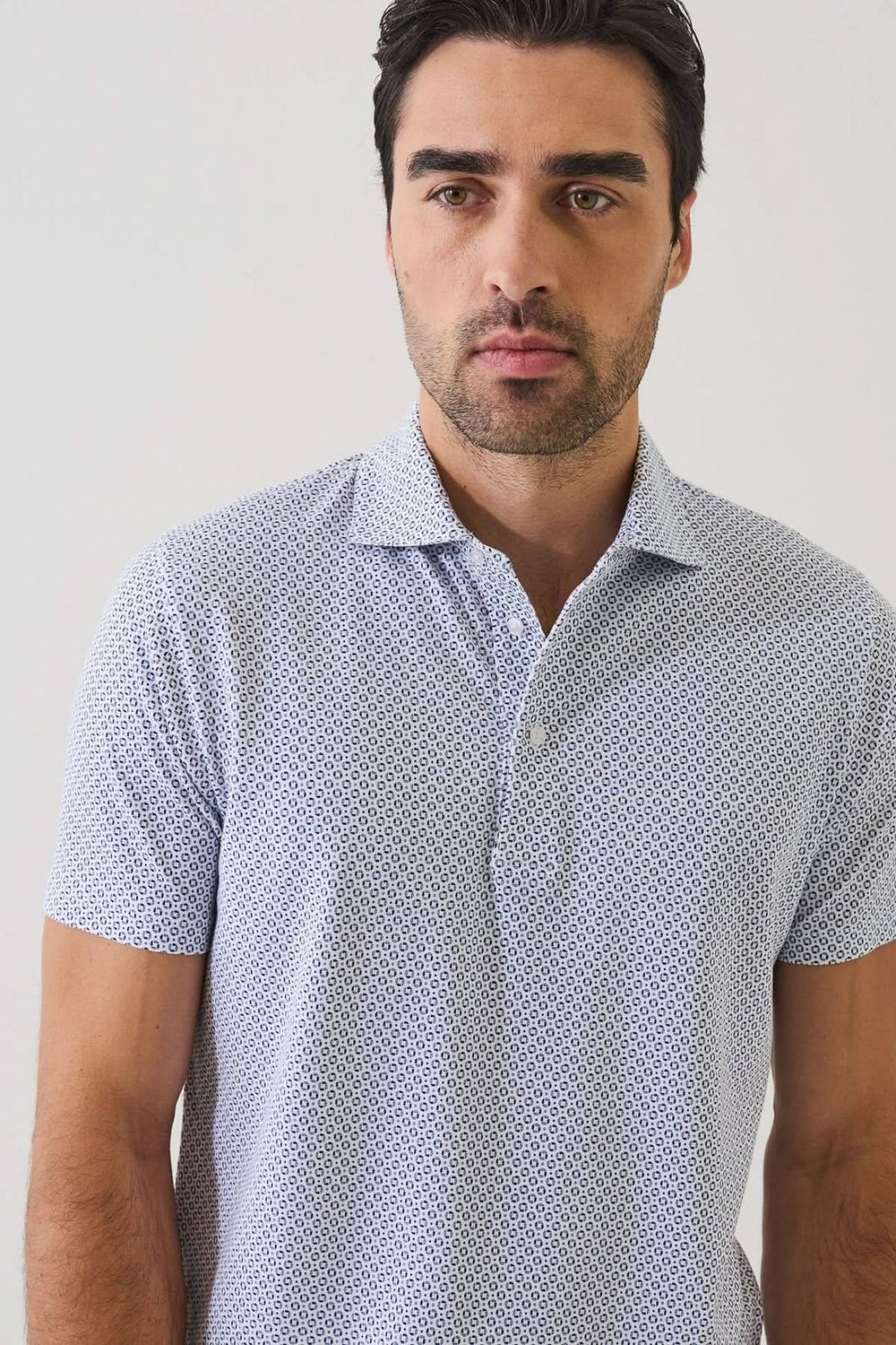 Homme portant un POLO IMPRIMÉ À MANCHES COURTES avec un motif géométrique discret et un col ouvert, idéal pour l'été.