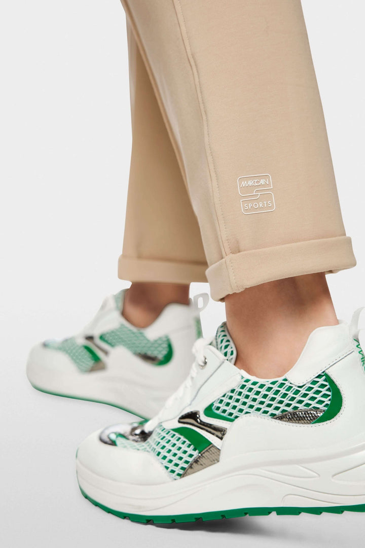 Pantalon FRIA à enfiler en mélange de coton beige, porté avec des baskets sports vertes et blanches, coupe droite légèrement fuselée.