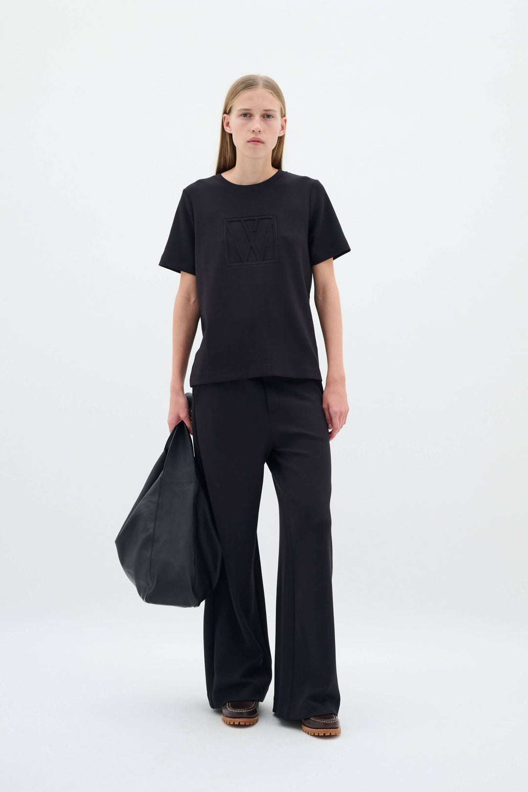 Femme portant un ensemble en noir avec un pantalon large et un tee-shirt, tenant un sac à main.