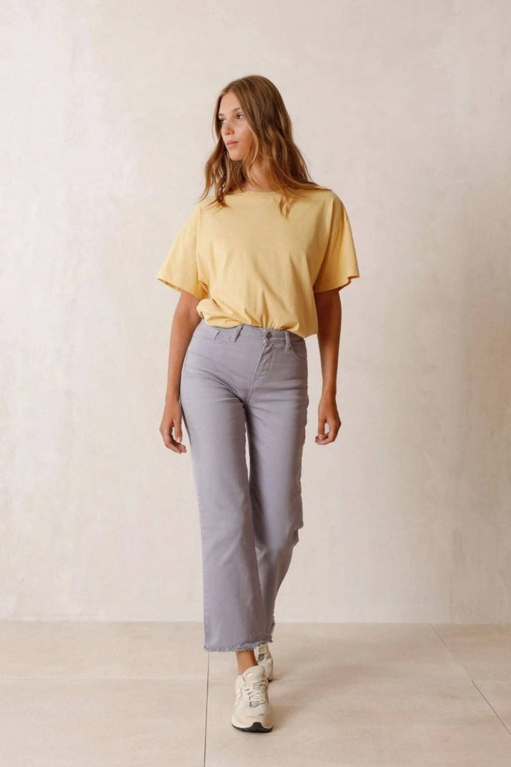 Femme en t-shirt jaune et pantalon gris décontracté marchant sur un fond neutre.