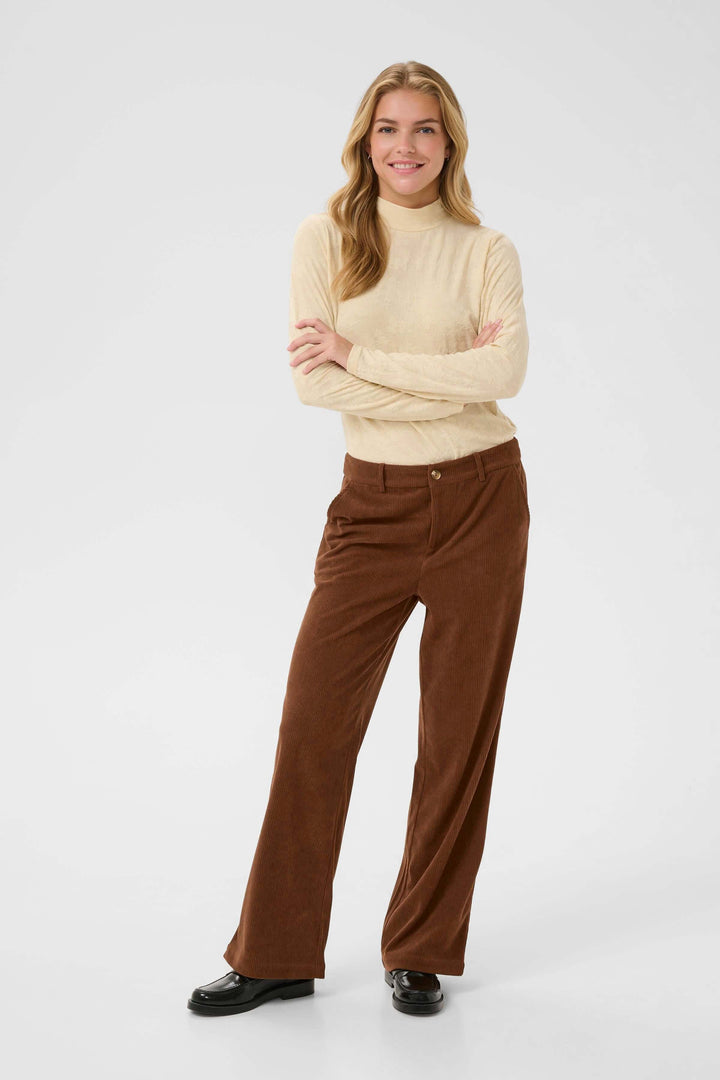 Femme portant le Pantalon Kanna en velours côtelé à jambe large, style moderne et élégant, couleur marron, avec pull crème.