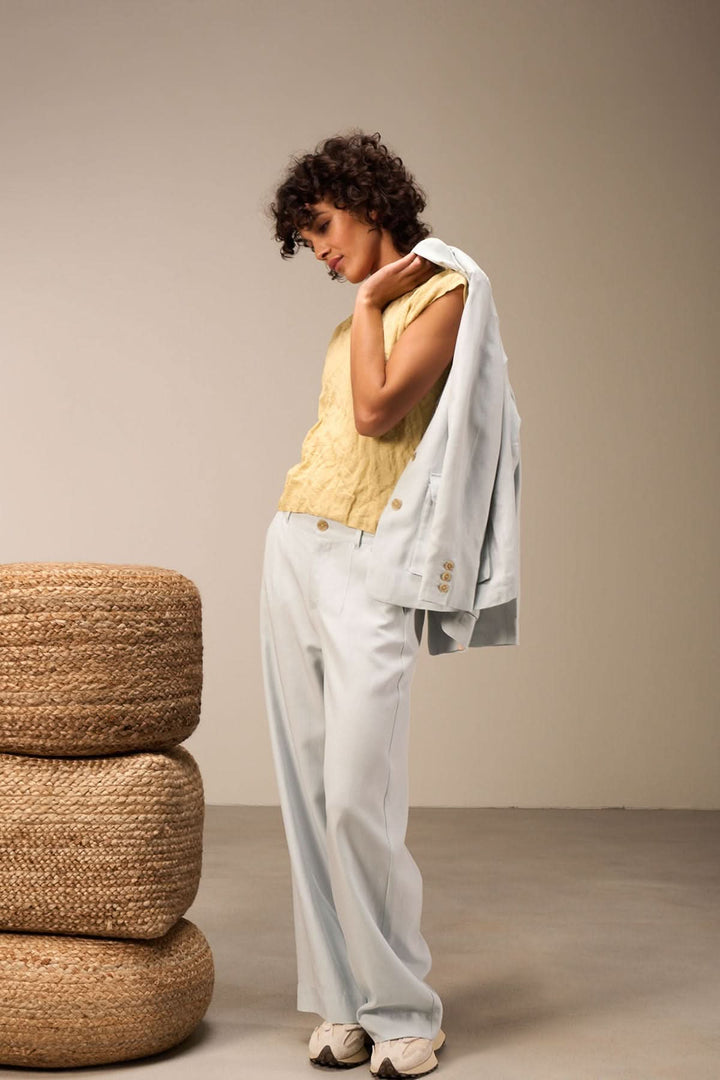 Femme portant un pantalon large bleu clair avec un haut jaune et une veste, posant élégamment.