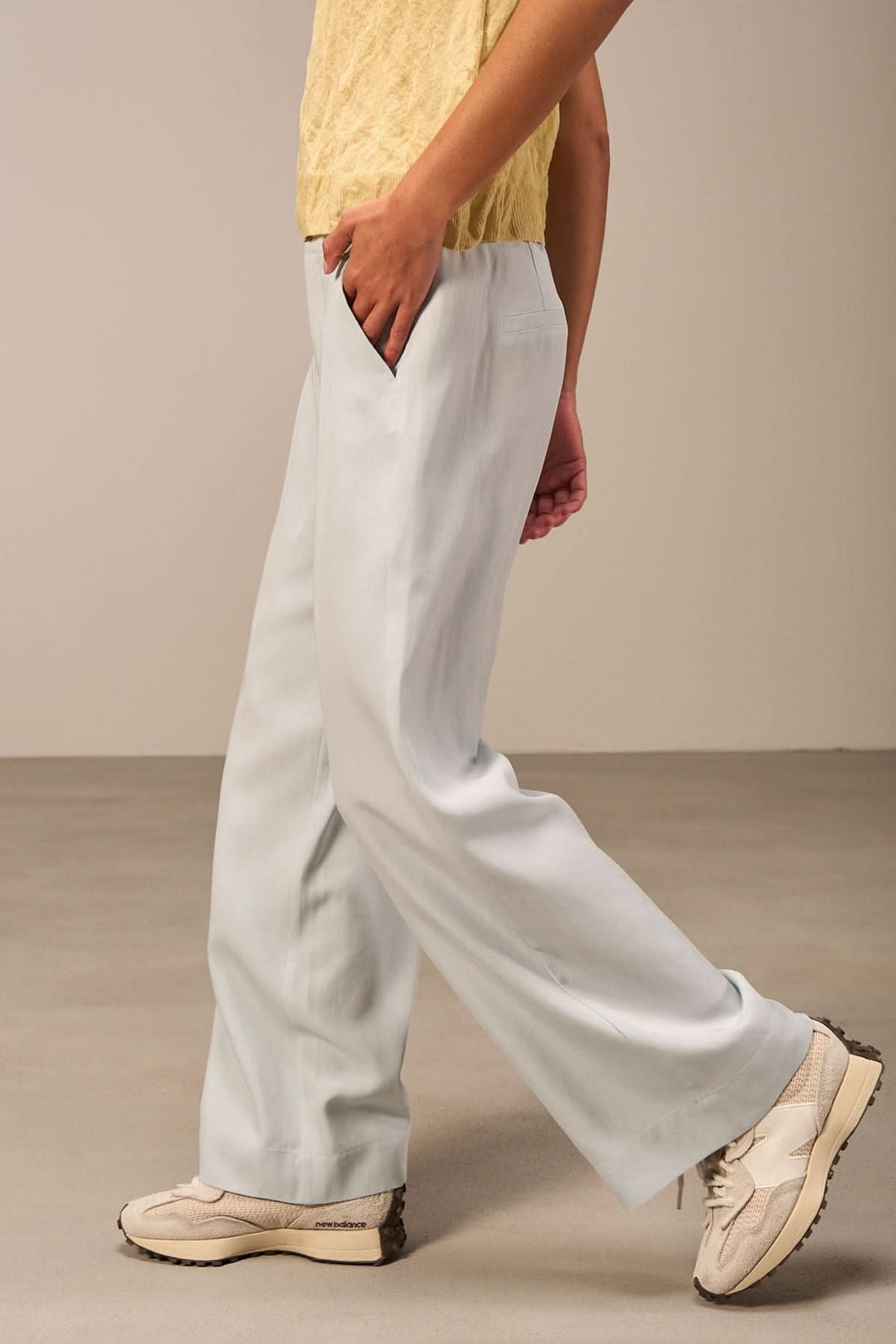 Pantalon large bleu clair avec taille haute, associé à un haut jaune et des chaussures blanches.