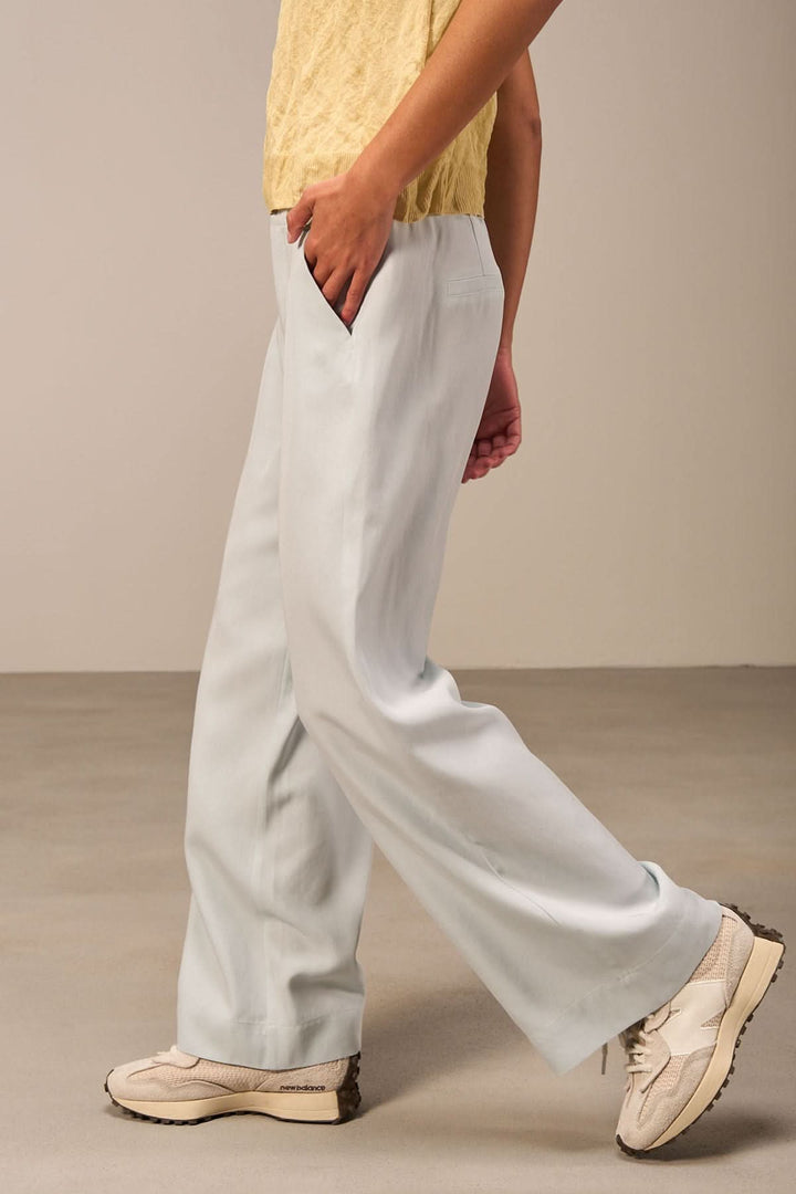Pantalon large bleu clair avec taille haute, associé à un haut jaune et des chaussures blanches.