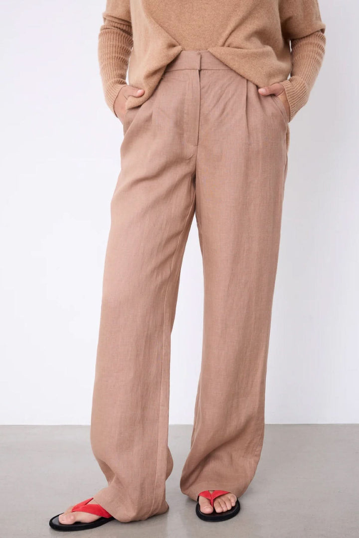 Pantalon Paula large fluide taille haute en tissu beige porté avec un pull beige et des sandales noires et rouges.