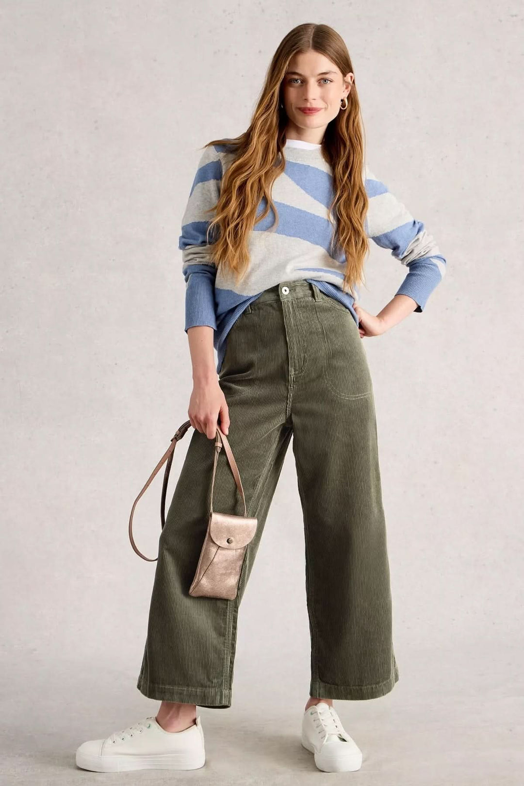 Pantalon Tia en velours côtelé avec coupe évasée, taille haute, porté avec un chandail rayé et des baskets blanches.