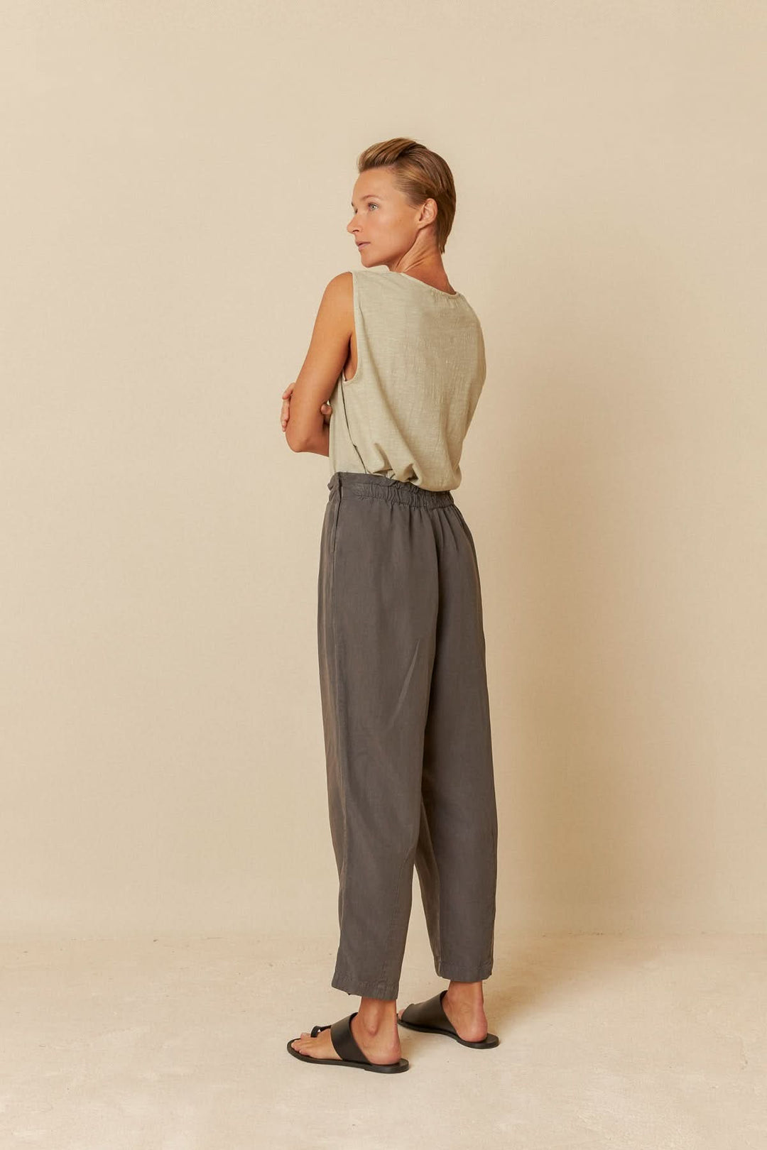 Femme portant un pantalon ample gris à taille élastiquée, vue de dos, sur fond neutre.