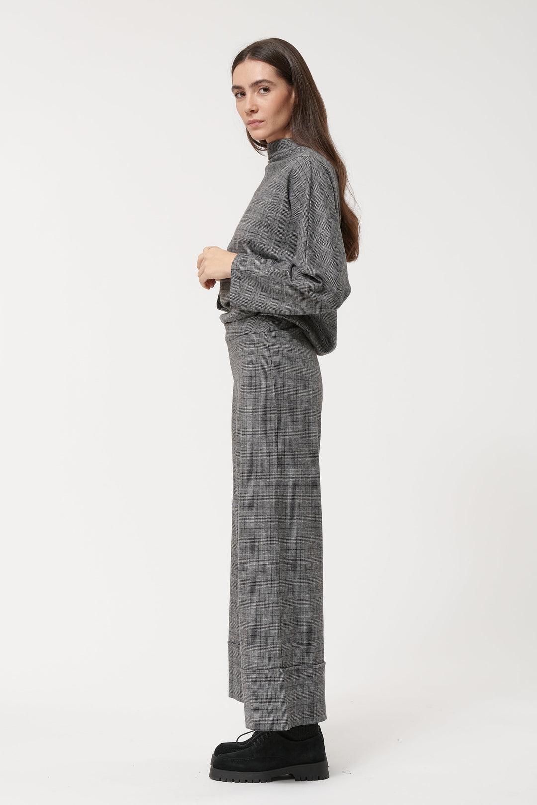 Pantalon à carreaux large et fluide avec taille haute, porté avec un pull gris, style chic et décontracté.