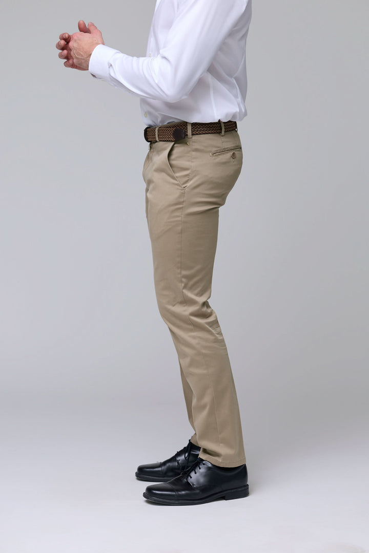 Homme portant un pantalon chino ajusté beige avec ceinture, chemise blanche et chaussures noires, vue de profil.