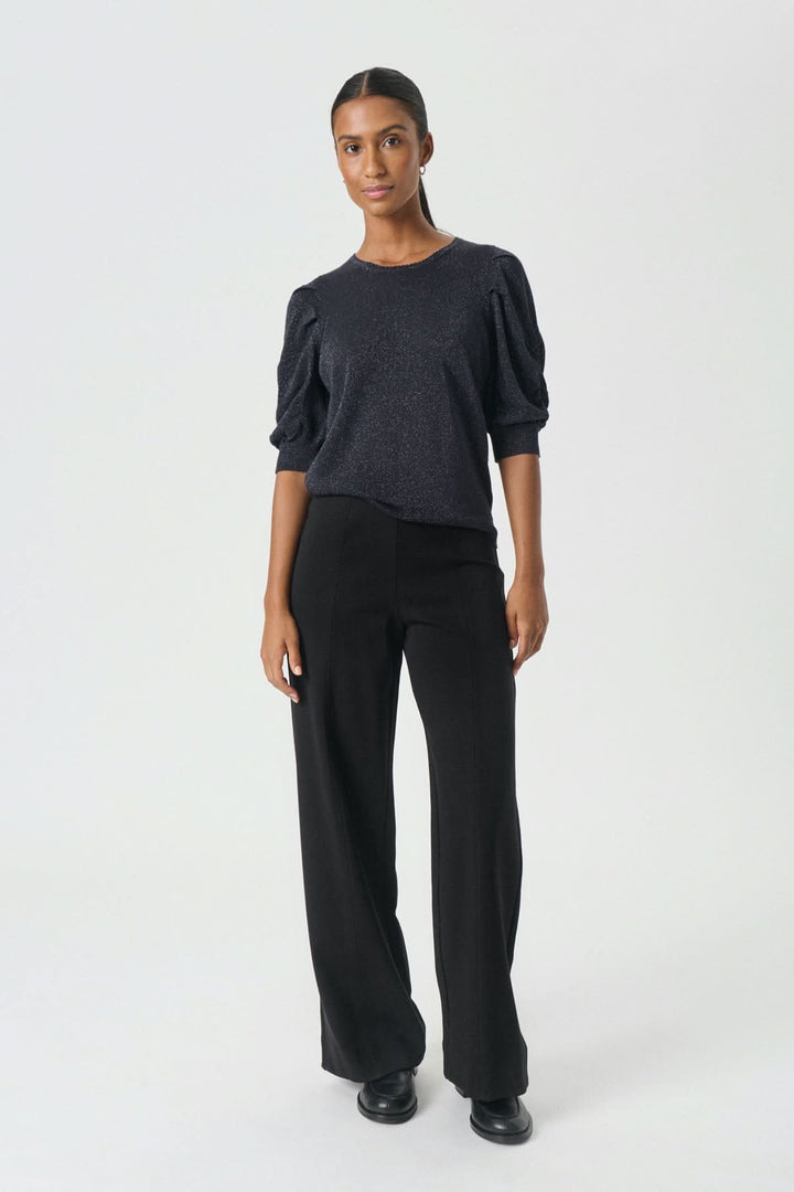 Femme portant le Pantalon classique Vinda, silhouette moderne et fluide avec jambe large pour confort au bureau ou sortie, couleur noire élégante.