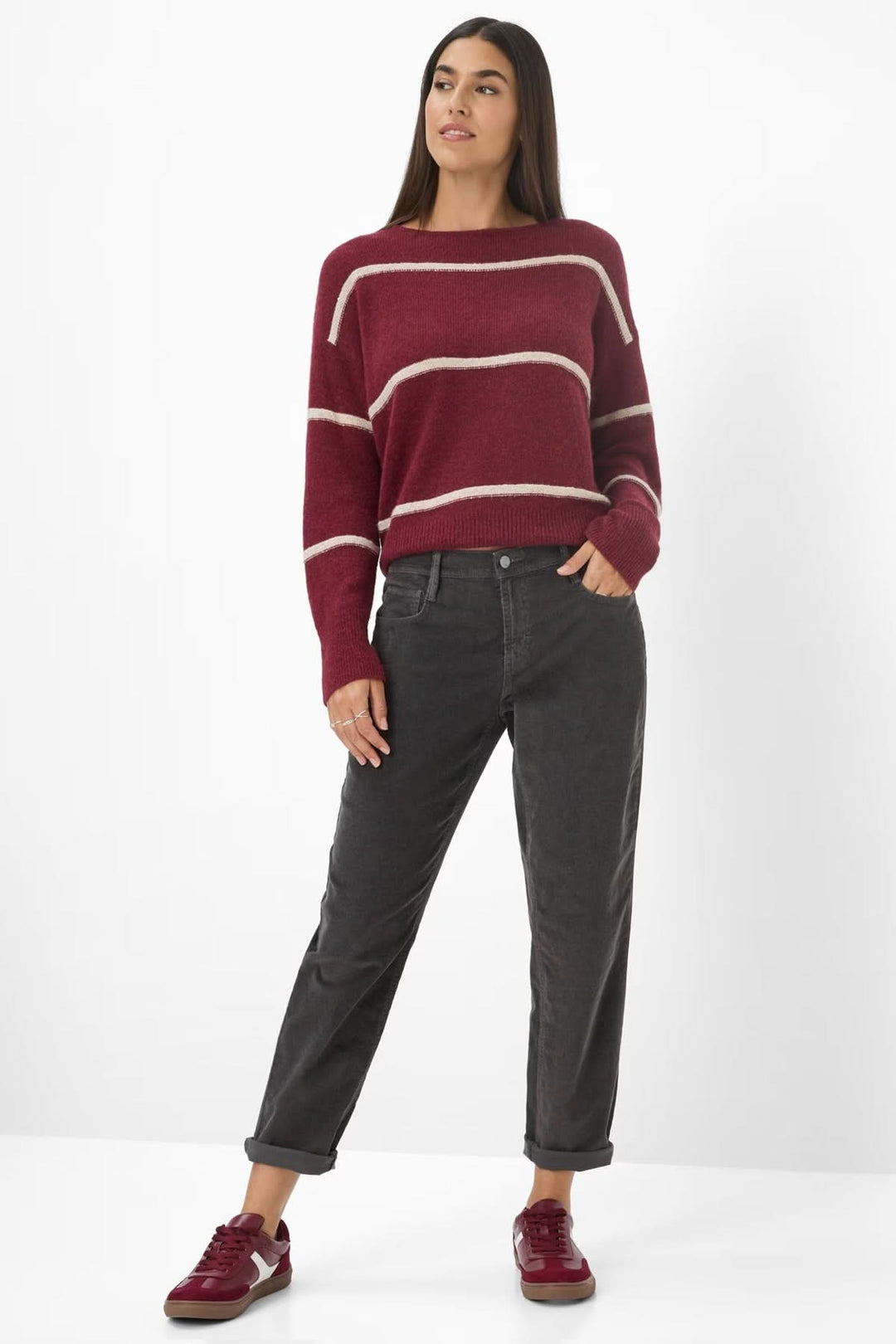 Femme portant un pull rayé bordeaux et un pantalon gris foncé, avec des baskets assorties, pour un look décontracté.