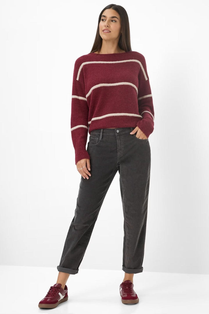 Femme portant un pull rayé bordeaux et un pantalon gris foncé, avec des baskets assorties, pour un look décontracté.