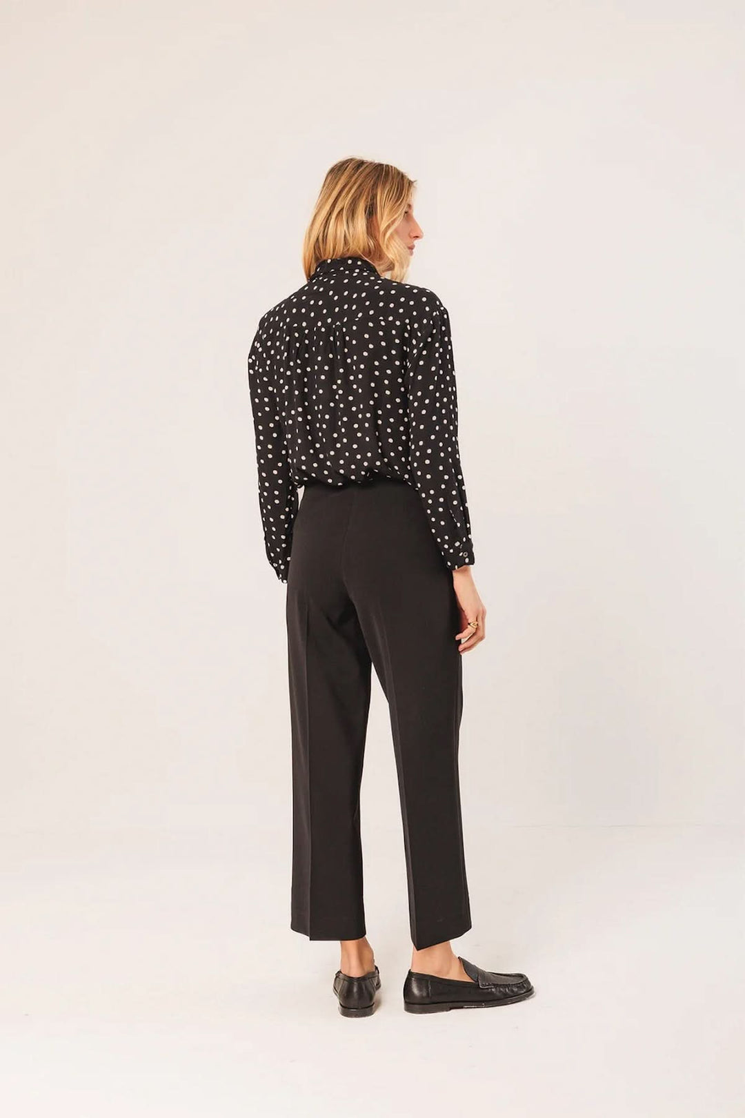 Vue arrière d'un pantalon droit à coupe fluide noir, porté avec une chemise à motifs et des chaussures élégantes.