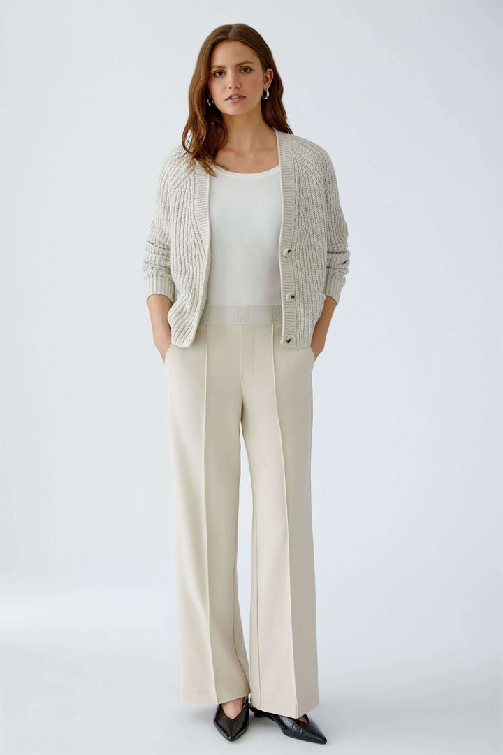 Femme portant un pantalon droit à taille élastique logo beige, style élégant et moderne avec plis marqués.