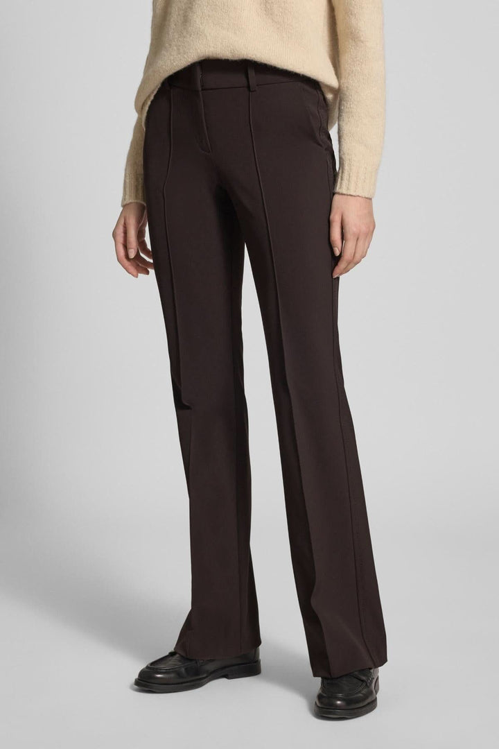 Pantalon droit évasé à plis marqués, coupe élégante et confortable, montré porté avec chandail beige et chaussures noires.