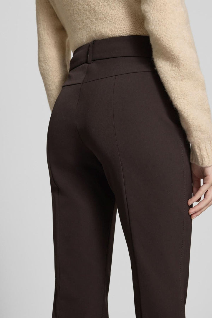 Vue arrière du pantalon droit évasé à plis marqués, taille mi-haute, en tissu marron, portant un chandail beige.