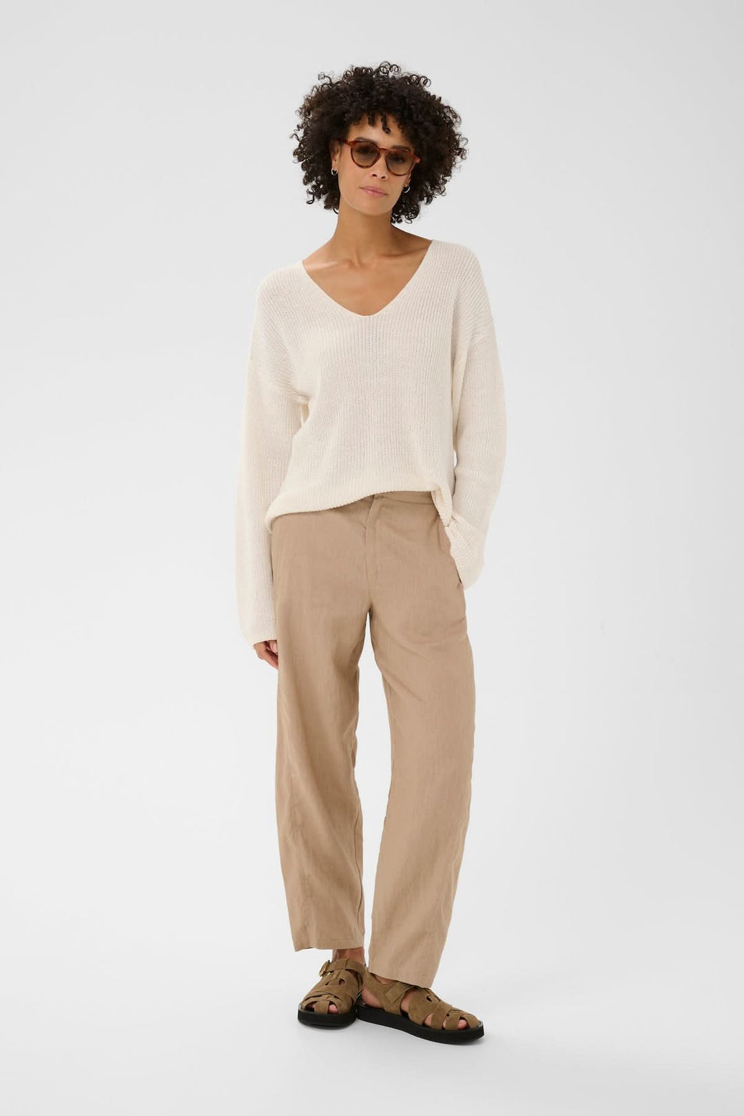 Modèle portant le Pantalon en lin Atima avec coupe droite et tissu léger, associé à un pull blanc décontracté et des sandales.