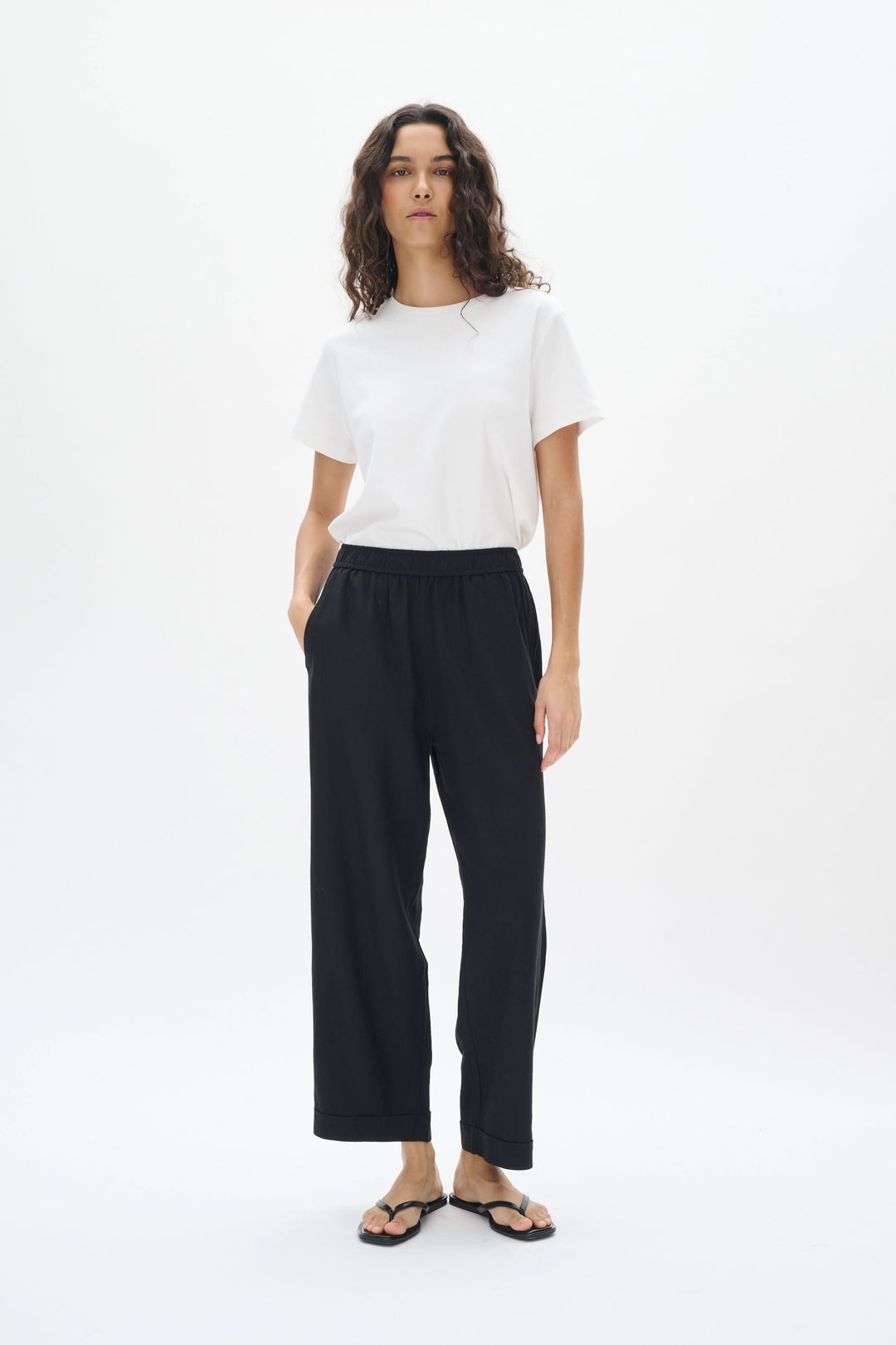 Femme portant un pantalon en lin noir avec taille élastique et t-shirt blanc, affichant un style décontracté.