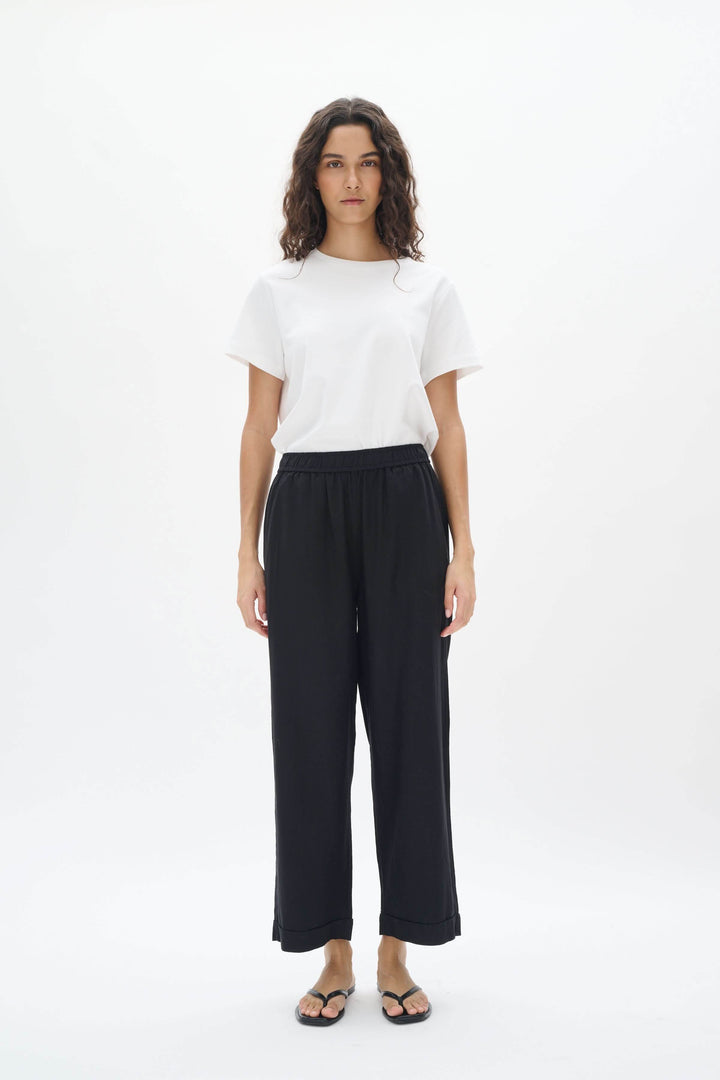 Femme portant un pantalon en lin noir avec taille élastique et t-shirt blanc, en pose debout.