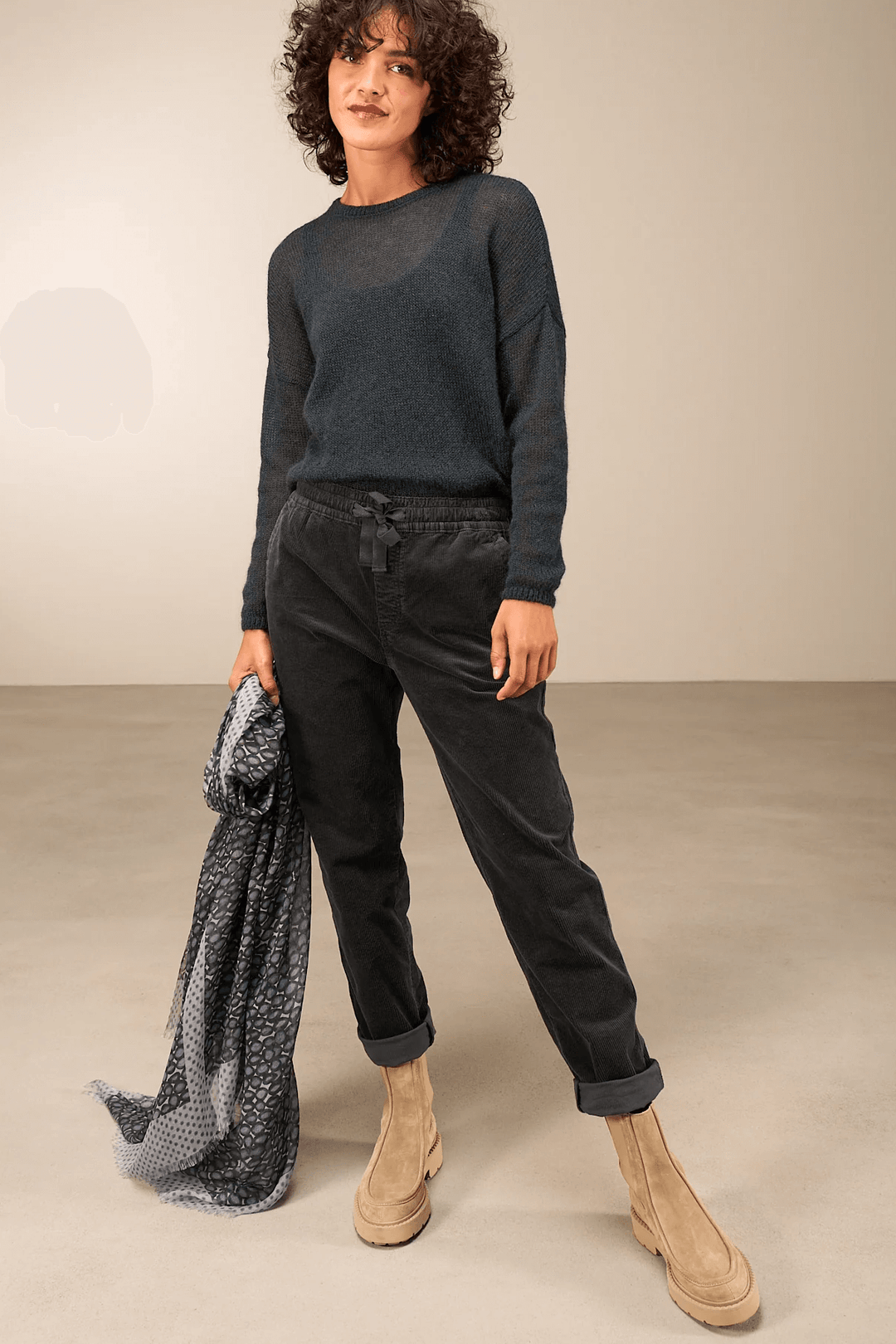 Femme portant un pantalon en velours côtelé noir avec taille élastique, accompagnée d'un chandail ample et bottes beiges.