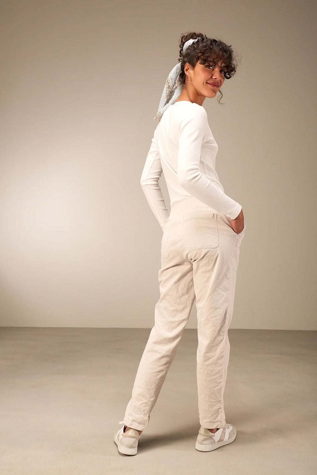 Woman wearing white casual outfit with hands in pockets, standing on beige background, showcasing comfortable style.