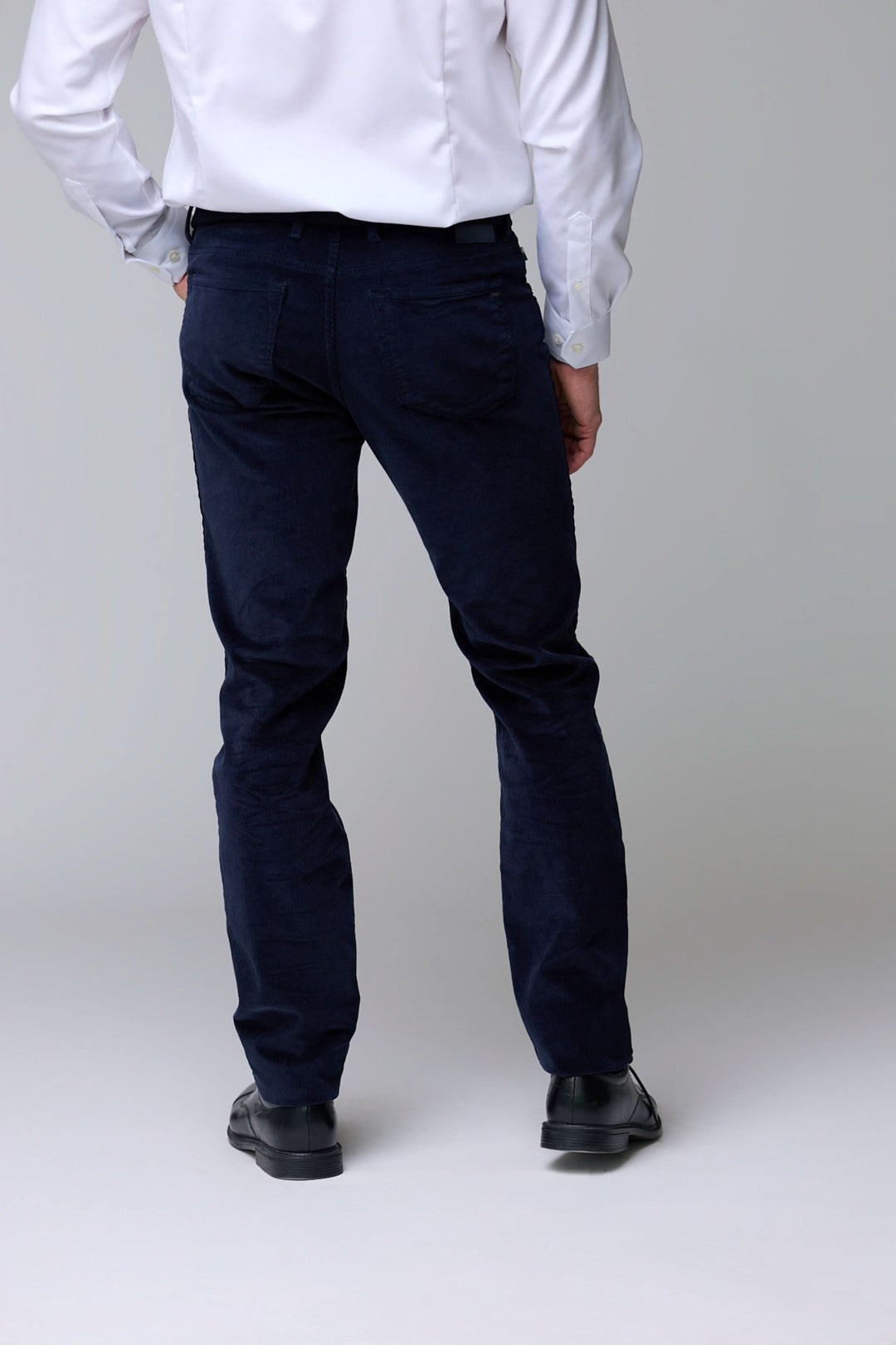 Homme portant un pantalon en velours côtelé bleu marine, coupe droite légèrement ajustée, avec une chemise blanche.