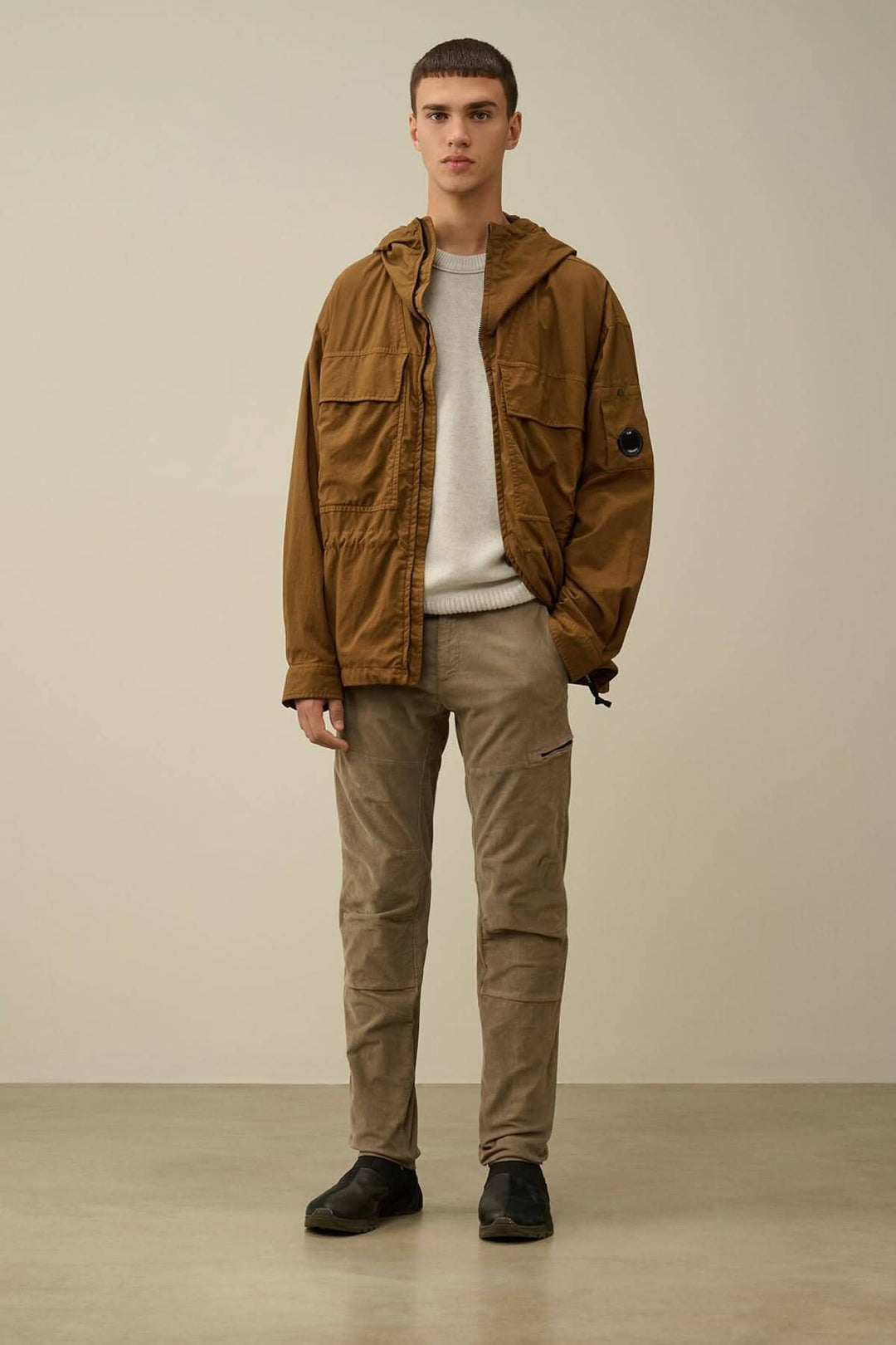 Homme portant un pantalon en velours côtelé beige avec une veste marron et un pull gris, photo en studio.
