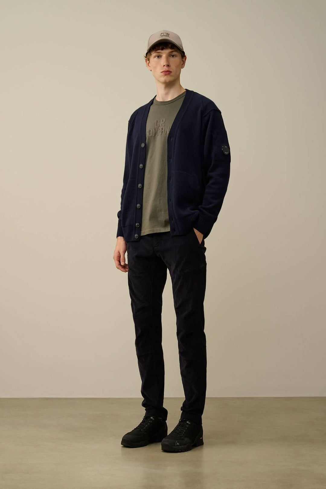 Homme portant un cardigan navy, t-shirt olive et pantalon noir, affichant un style décontracté moderne.