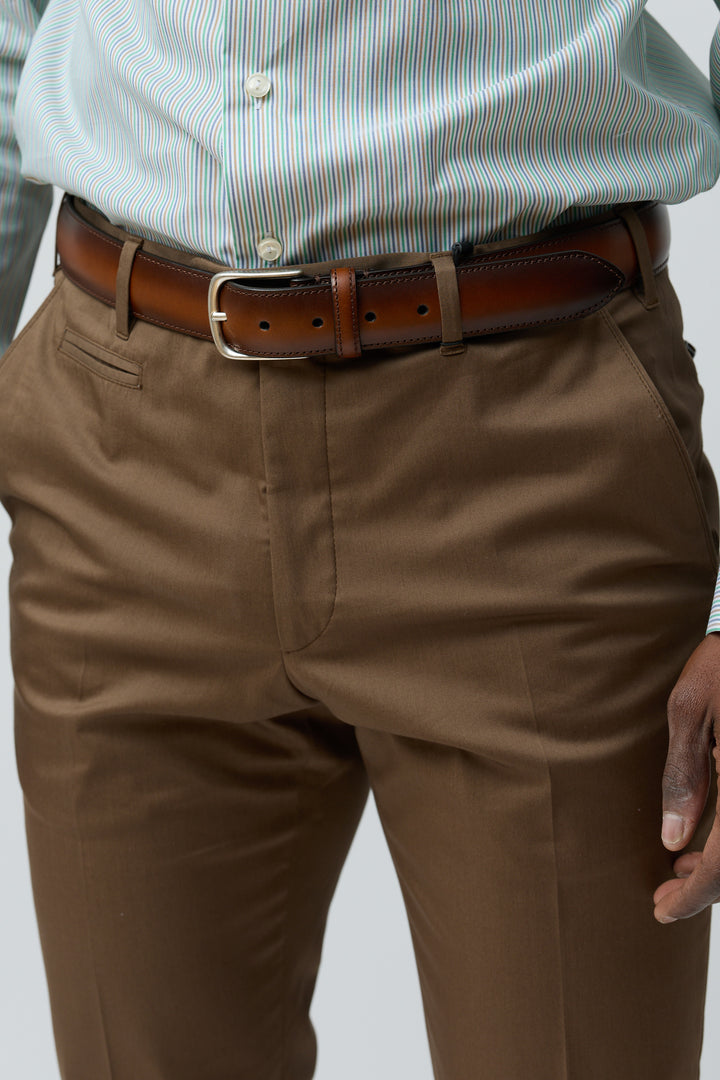 Pantalon habillé coupe ajustée marron porté avec chemise rayée et ceinture en cuir marron, style polyvalent et élégant.