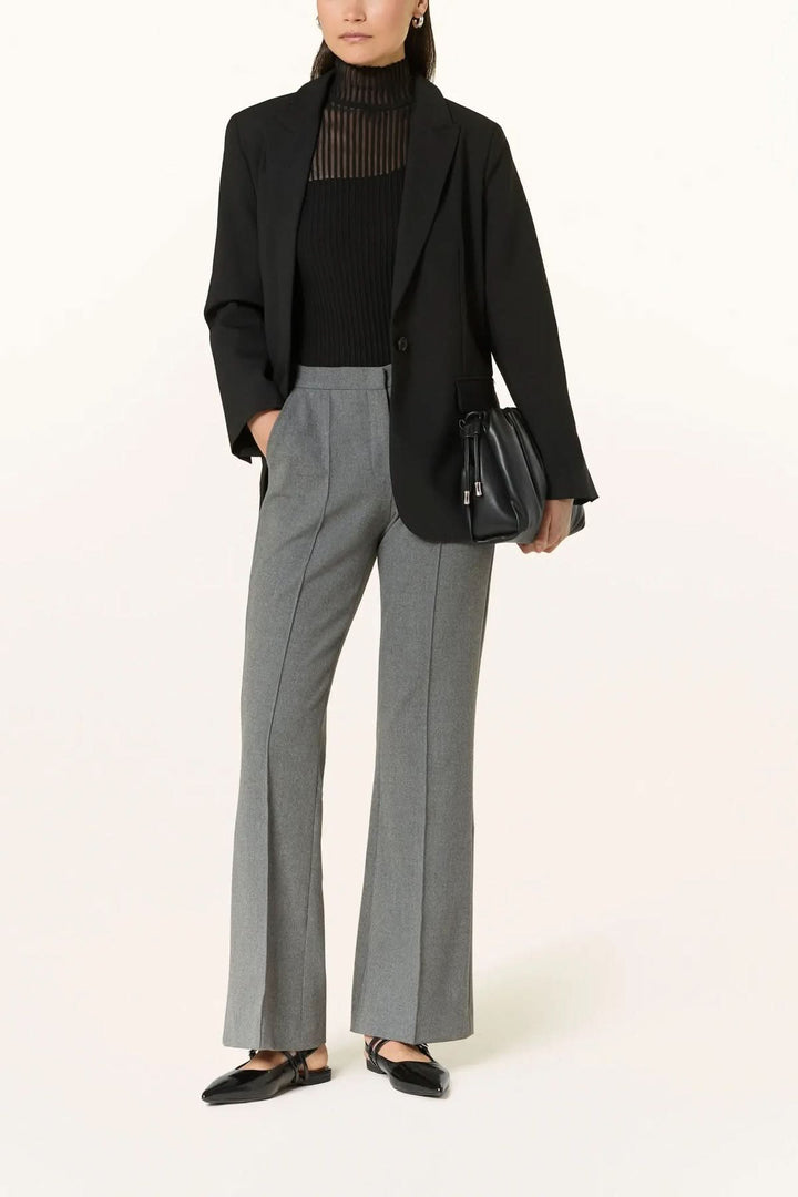 Pantalon habillé coupe évasée à plis marqués porté avec un blazer noir, haut col roulé et chaussures noires élégantes.