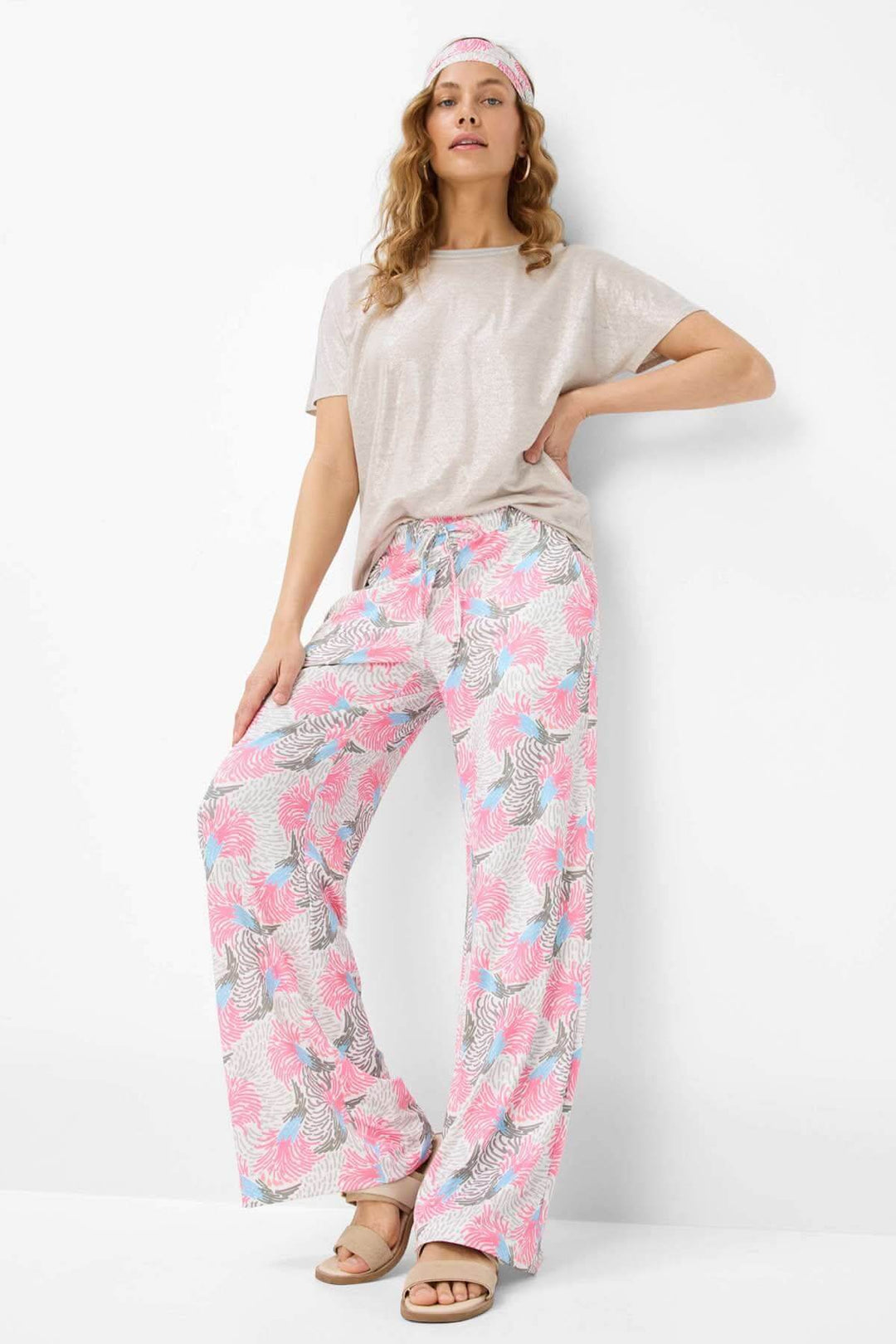Pantalon imprimé MAINE avec motif tropical en rose, bleu clair et vert, porté avec un top beige et bandeau.
