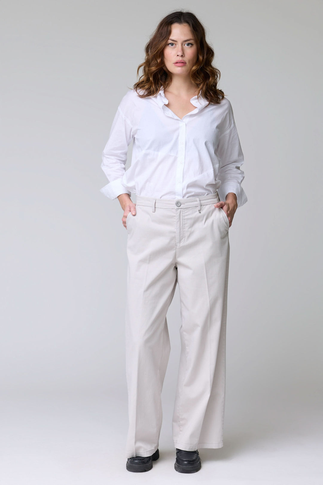 Femme portant un pantalon à jambe large blanc, debout avec une chemise blanche élégante.